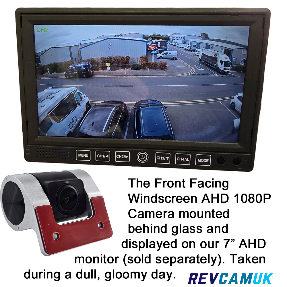 Front-facing AHD 1080P windscreen camera mounted behind glass, shown with real-world footage on a 7-inch AHD monitor (sold separately), demonstrating image quality on a dull, gloomy day